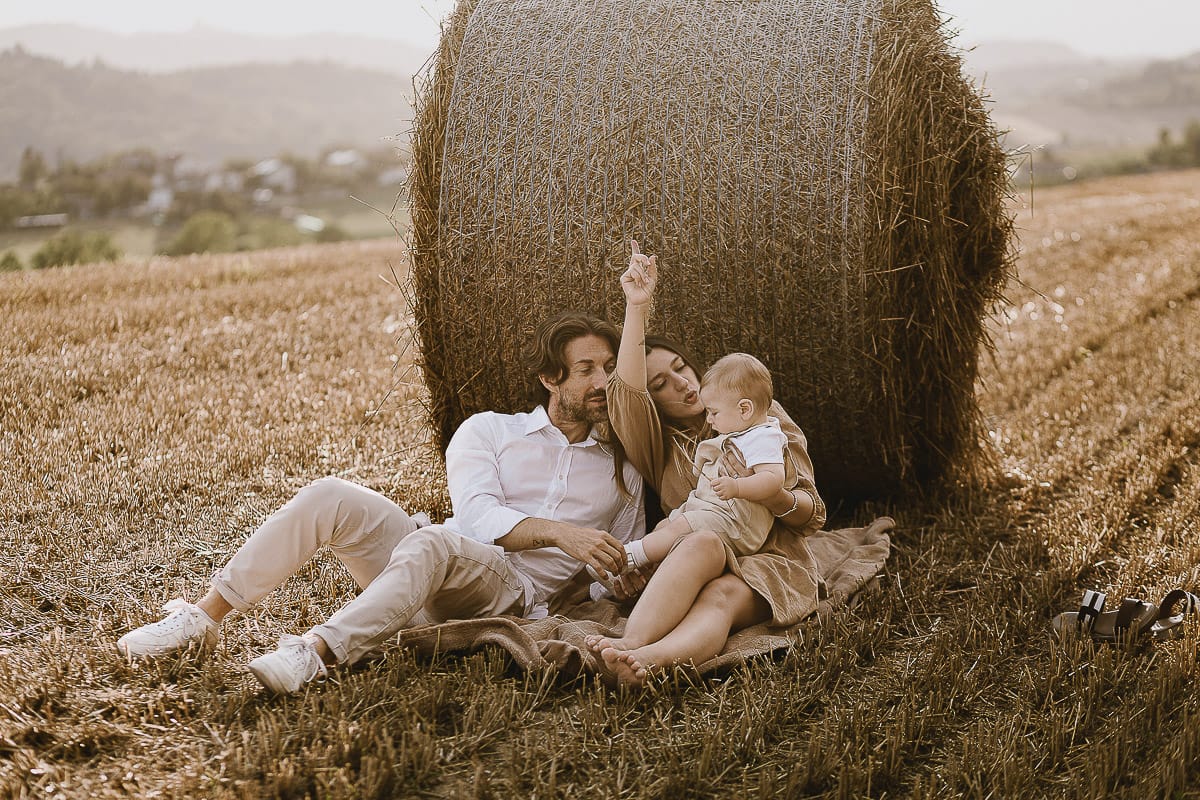Servizio fotografico di famiglia a Torino: un tramonto dorato a Mombello di Torino. Chiara, Alessandro e il piccolo Leonardo distesi in un campo davanti ad una balla di fieno.