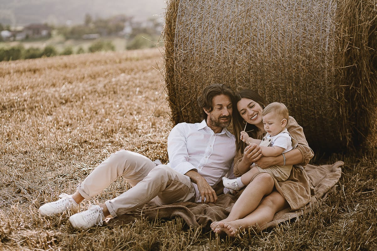 Servizio fotografico di famiglia a Torino: un tramonto dorato a Mombello di Torino. Chiara, Alessandro e il piccolo Leonardo distesi in un campo davanti ad una balla di fieno.