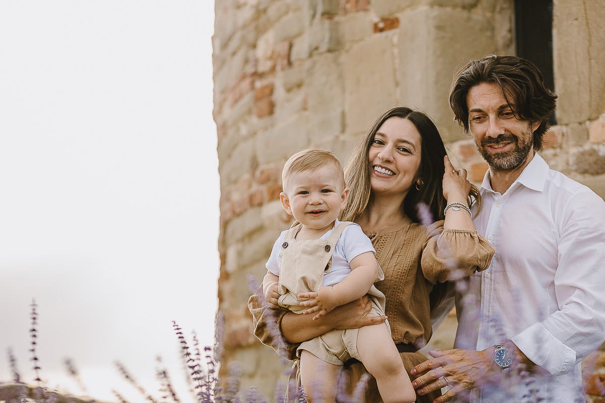 Servizio fotografico di famiglia a Torino: un tramonto dorato a Mombello di Torino. Chiara, Alessandro e leonardo in mezzo ad un cespuglio di fiori di colore lilla davanti alla chiesa romanica di San Lorenzo