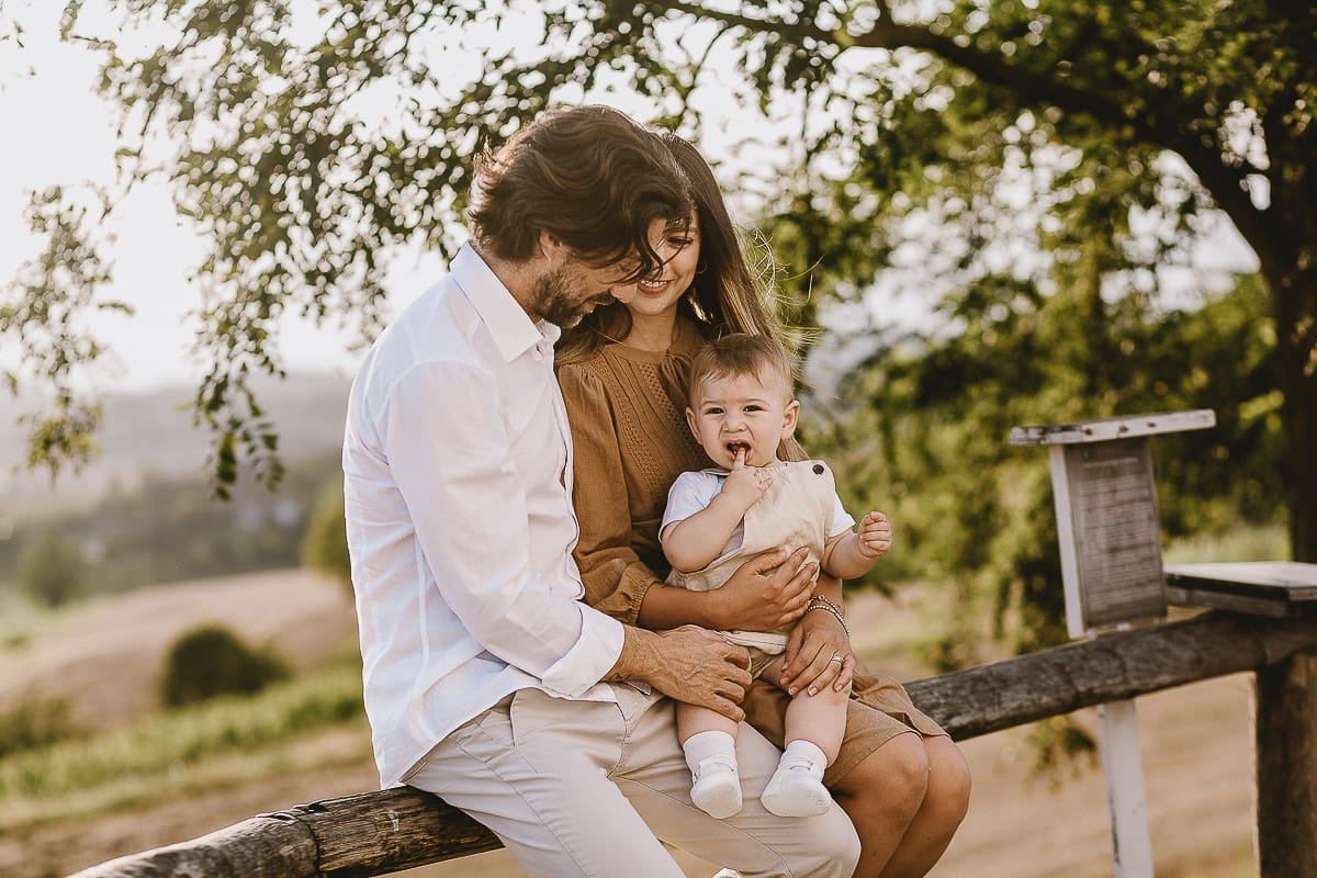 Servizio fotografico di famiglia a Torino: un tramonto dorato a Mombello di Torino. Chiara, Alessandro e il piccolo Leonardo seduti su di una staccionata