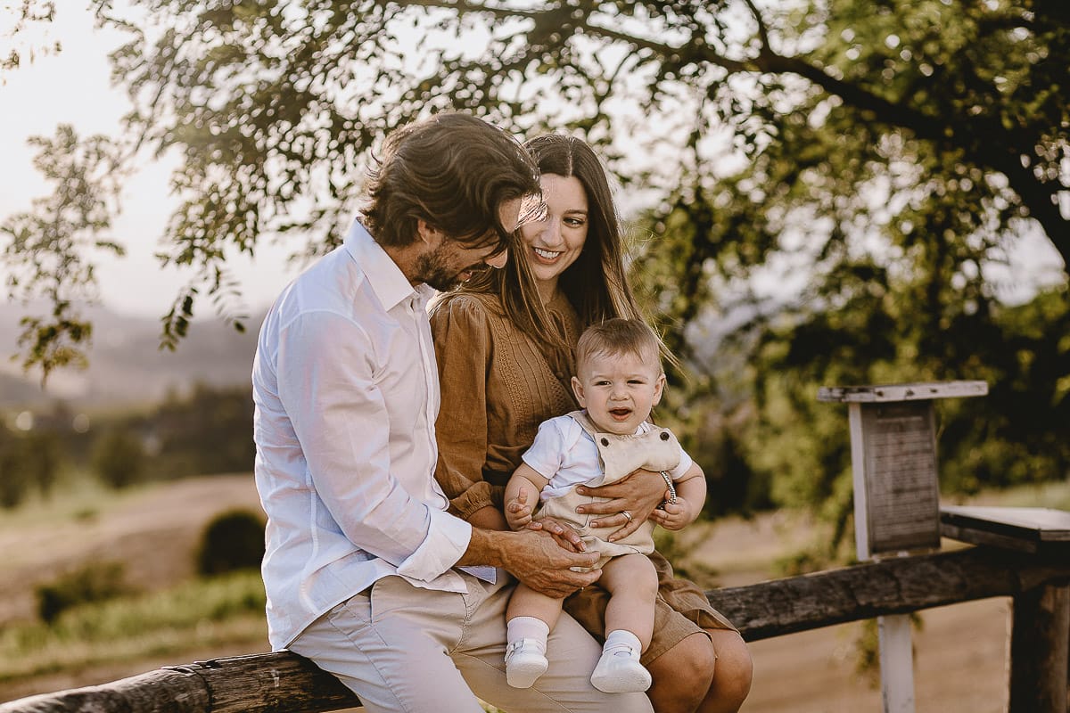 Servizio fotografico di famiglia a Torino: un tramonto dorato a Mombello di Torino. Chiara, Alessandro e il piccolo Leonardo seduti su di una staccionata