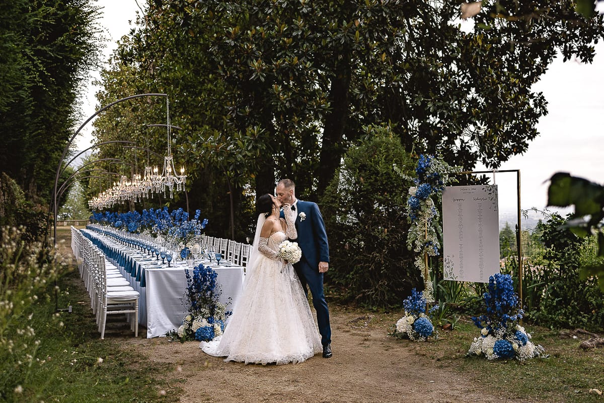 Matrimonio da favola al castello Canalis. sposi si baciano davanti al tavolo imperiale con lampadari a goccia, fiori, tovaglioli e bicchieri blu.