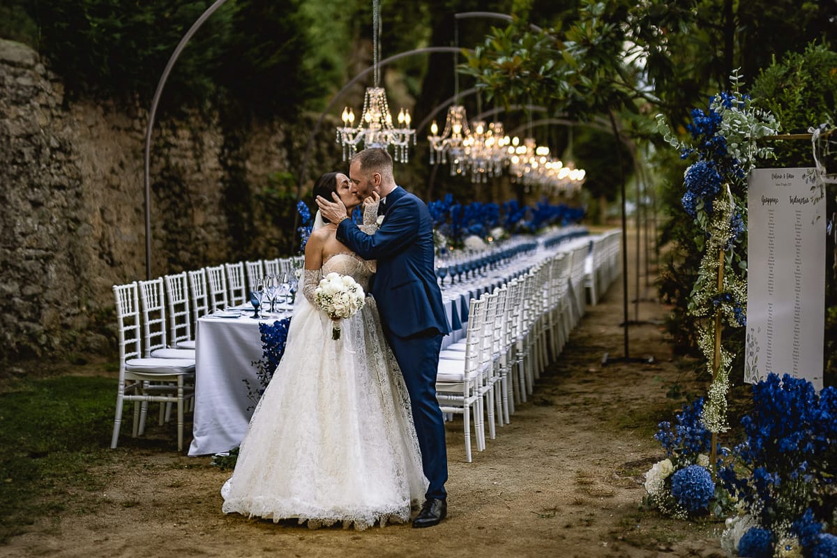 Matrimonio da favola al castello Canalis. sposi si baciano davanti al tavolo imperiale con lampadari a goccia, fiori, tovaglioli e bicchieri blu.