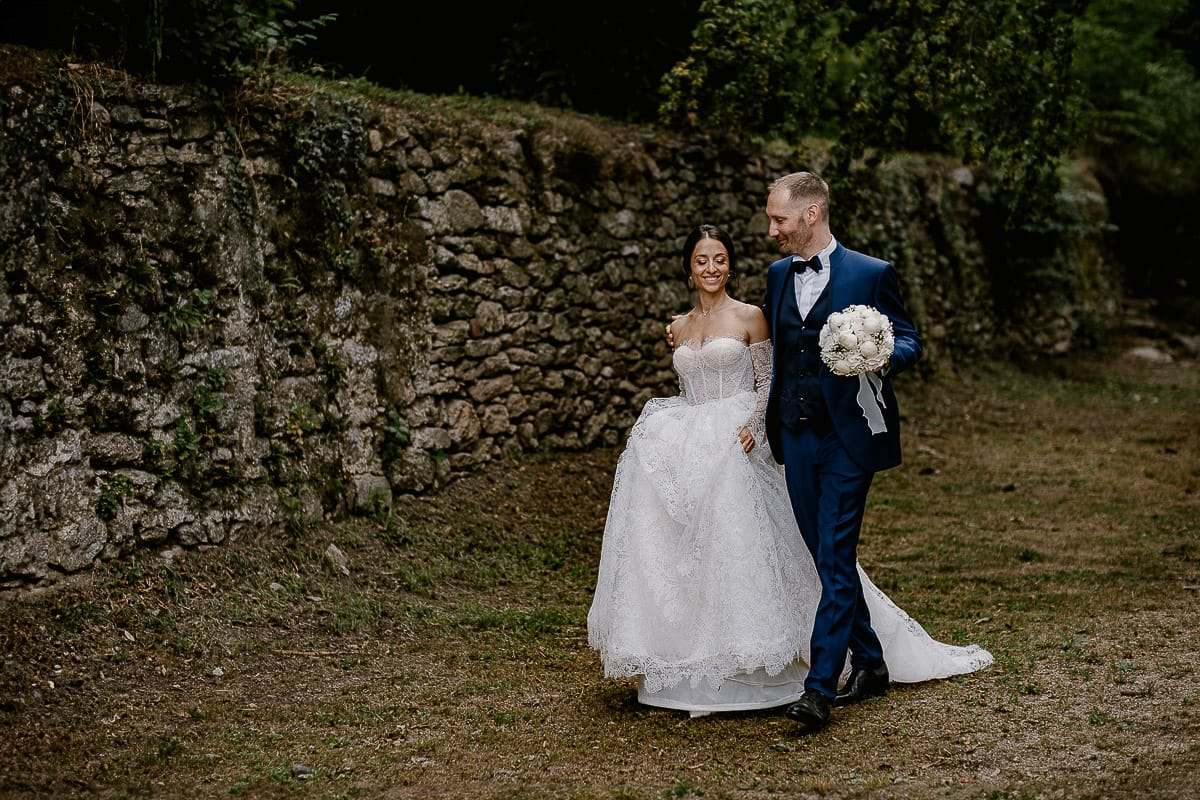 Matrimonio da favola al castello Canalis. Ritratto degli sposi nel bosco che camminano. sposo tiene in mano il bouquet della sposa.