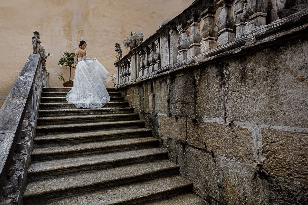 Matrimonio da favola al castello Canalis. Aperitivo. Foto della sposa che sale la scalinata di pietra danzando con l'abito.