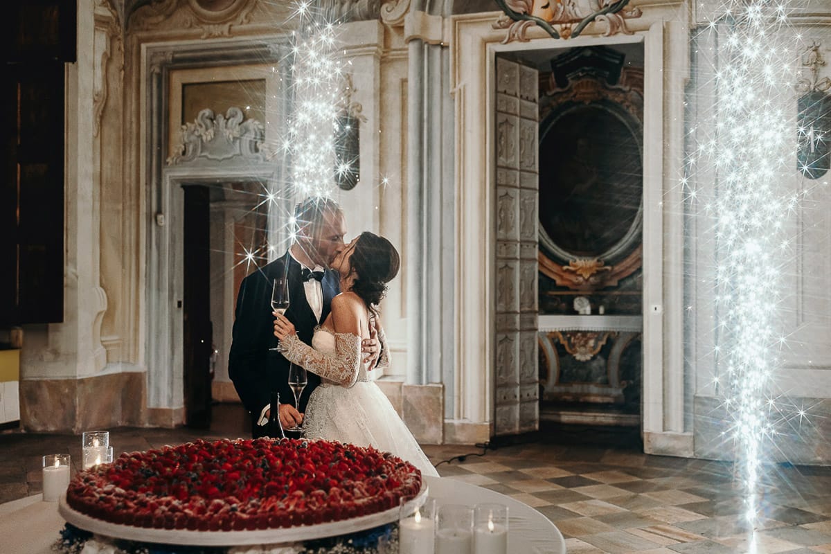 Matrimonio da favola al castello Canalis. Ricevimento. Taglio della torta. sposi si baciano nel salone delle feste, affrescato, dietro la crostata nuziale di Fabrizio Racca. Fontane luminose.