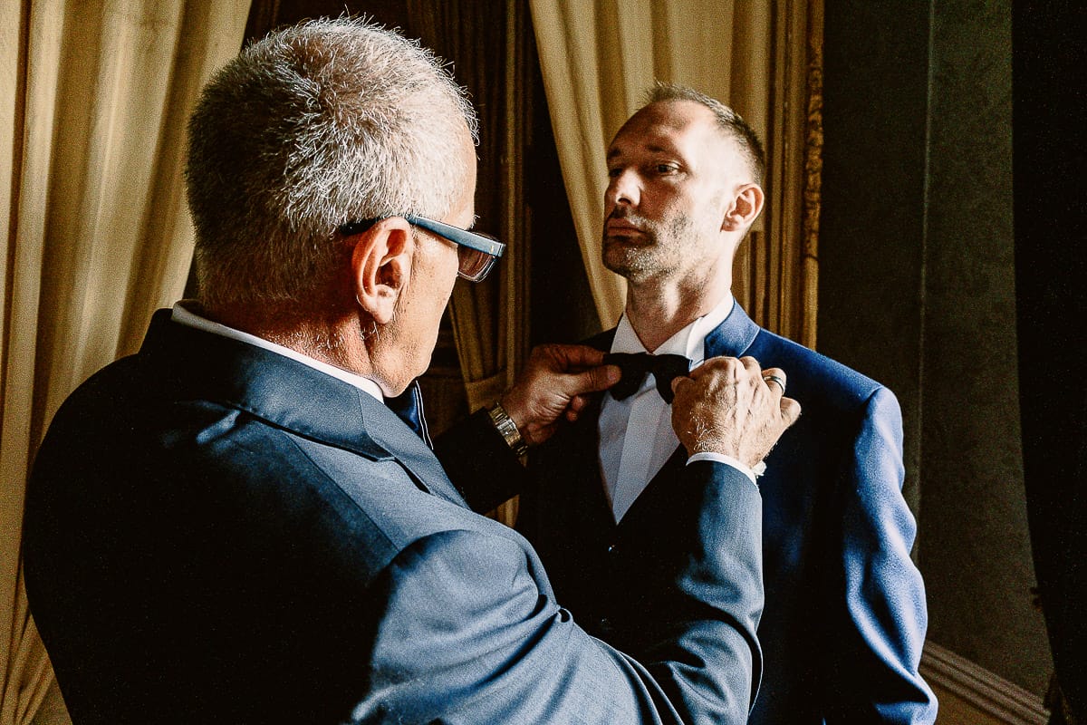 Matrimonio da favola al castello Canalis. Preparazione dello sposo. Padre sistema il papillon allo sposo.