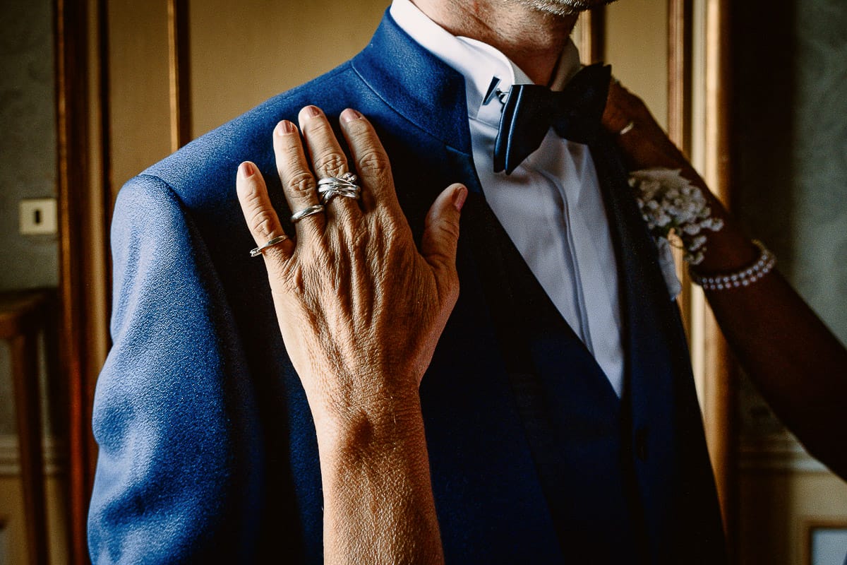 Matrimonio da favola al castello Canalis. Preparazione dello sposo. Madre sistema la giacca allo sposo.