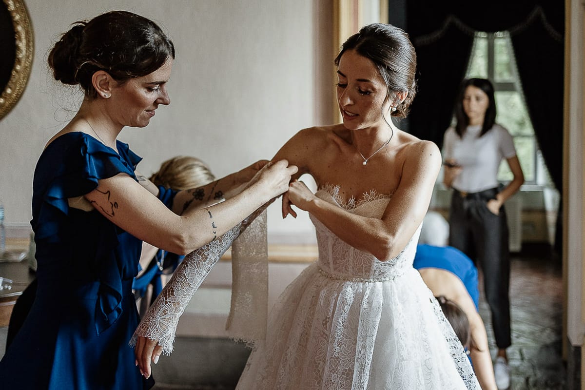 Matrimonio da favola al castello Canalis. Preparazione della sposa. Vestizione della sposa. la damigella infila la manica di pizzo alla sposa