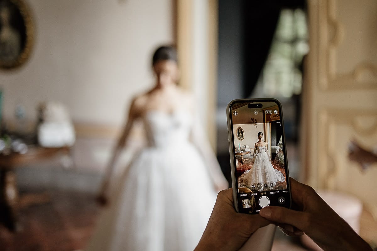 Matrimonio da favola al castello Canalis. Preparazione della sposa. Vestizione della sposa. Una damigella fa una foto alla sposa con il cellulare.