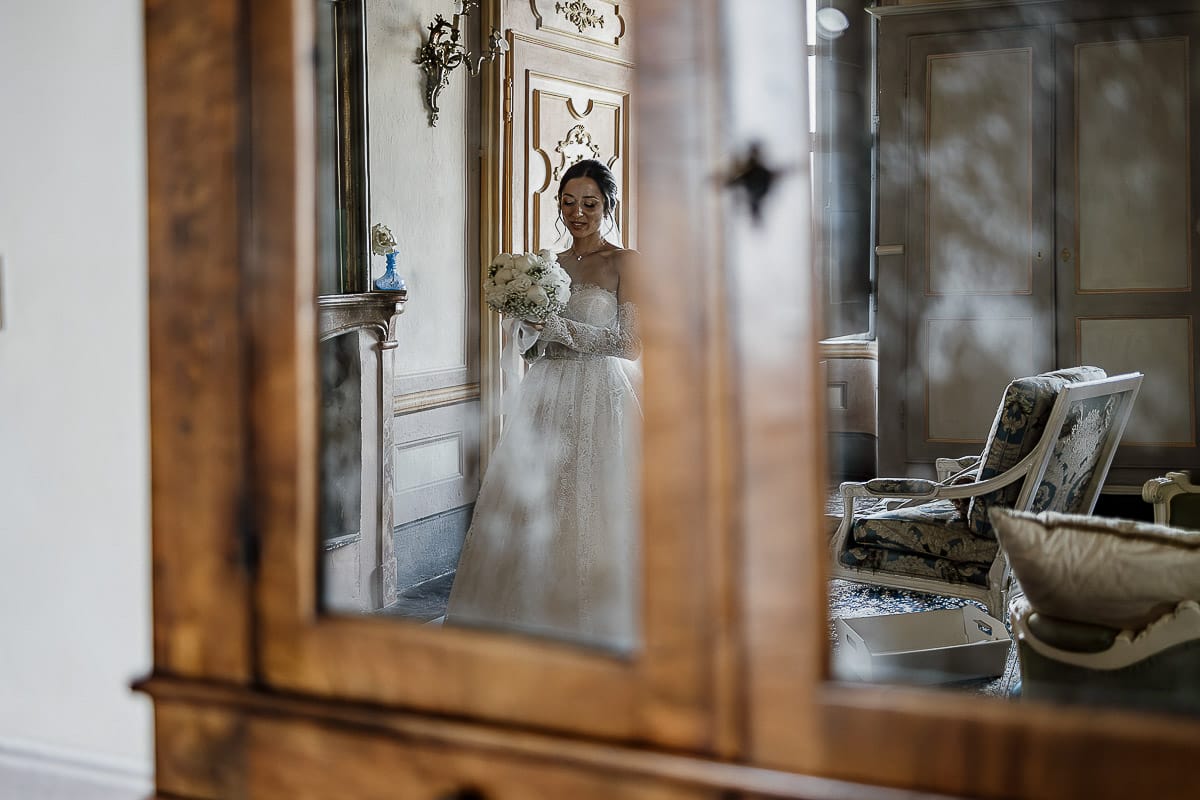 Matrimonio da favola al castello Canalis. Preparazione della sposa. Ritratto della sposa riflessa nella vetrata di un antico trumeau.