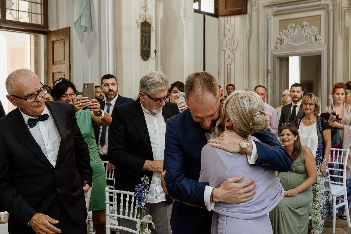 Matrimonio da favola al castello Canalis. Cerimonia. Sposo abbraccia la mdre. padre guarda.