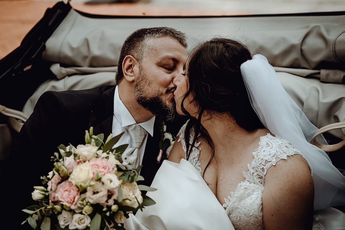 Matrimonio a Riva presso Chieri. Ritratti degli sposi. Sposi in auto, un maggiolino d'epoca bianco, si baciano