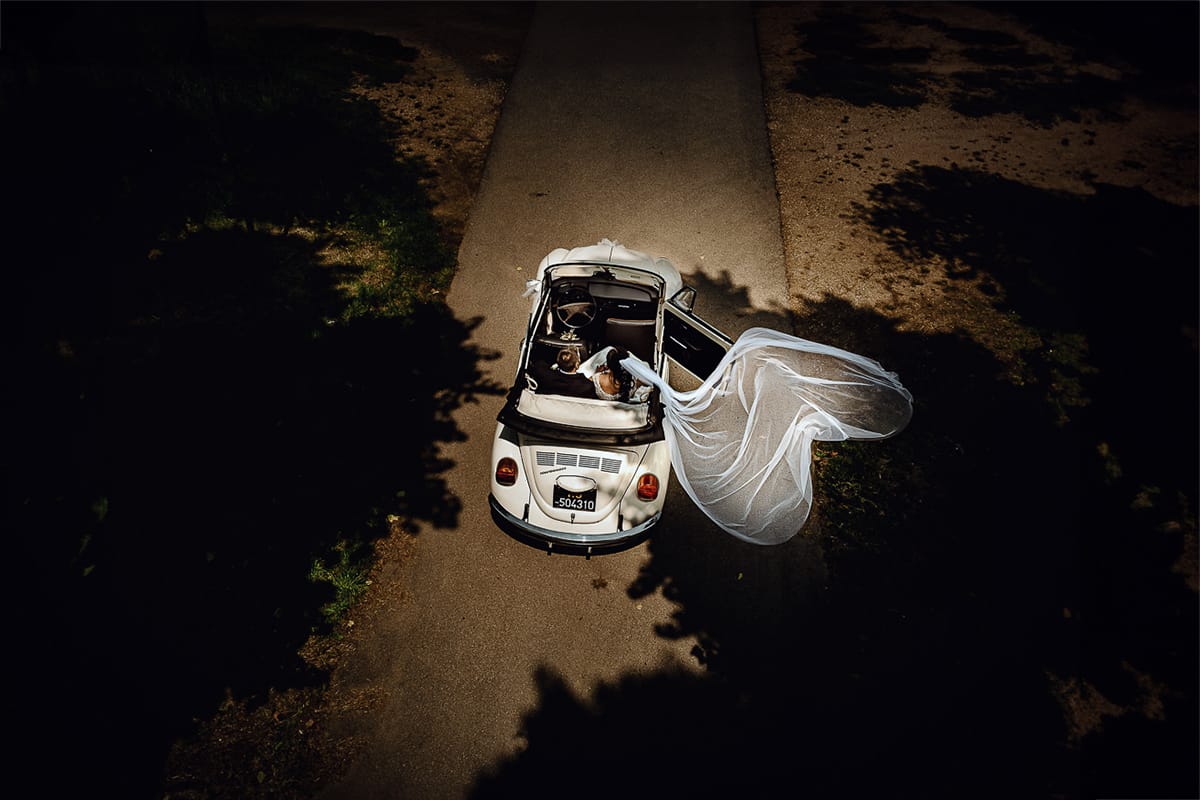 Matrimonio a Riva presso Chieri. Ritratti degli sposi. Sposi in auto, un maggiolino bianco d'epoca decappottabile. Il velo che vola sembra formare un cuore. Foto ripresa dal drone.