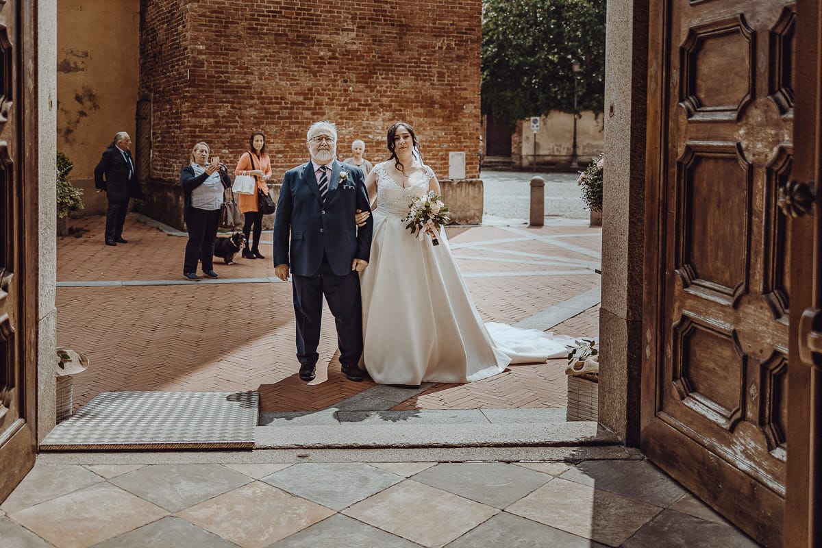 Matrimonio a Riva presso Chieri. Cerimonia. Sposa con il padre davanti all'entrata della chiesa..