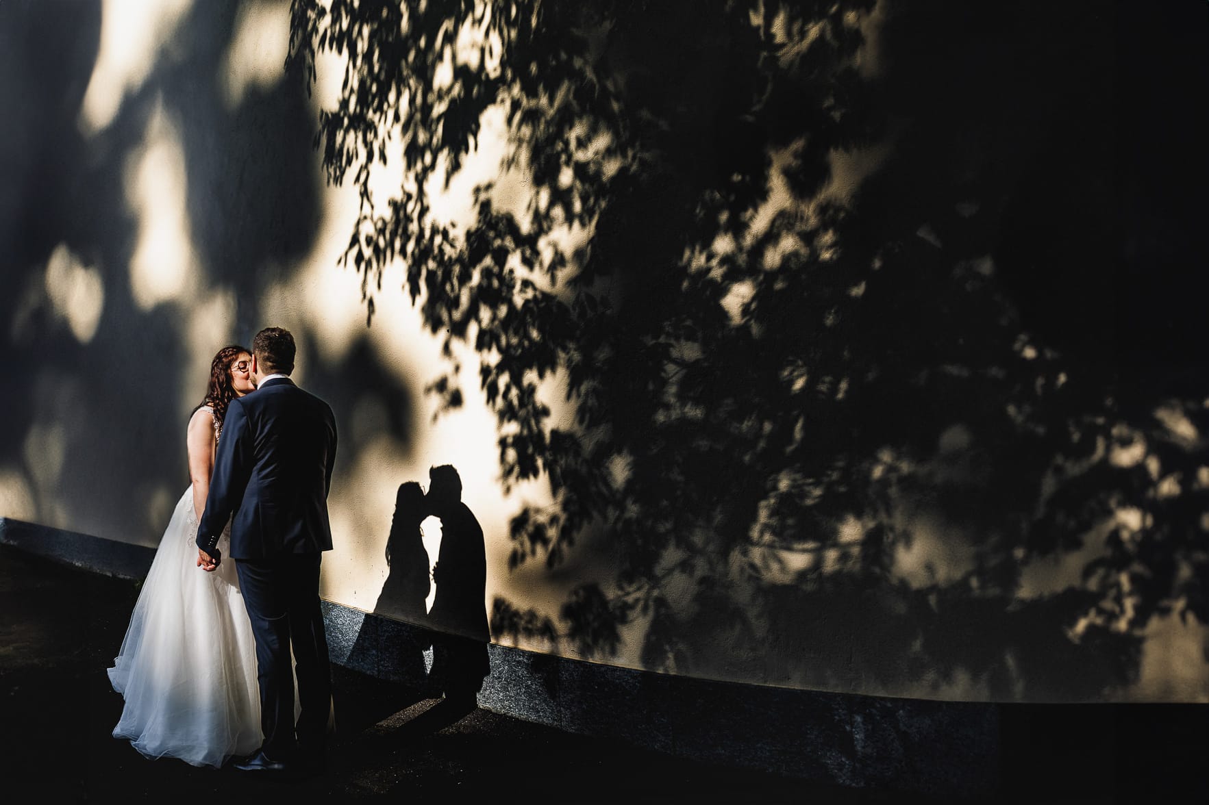 Matrimonio a San Mauro Torinese. Sessione di coppia. Sposi di fronte ad un muro dove si creano delle bellissime ombre degli sposi e degli alberi.