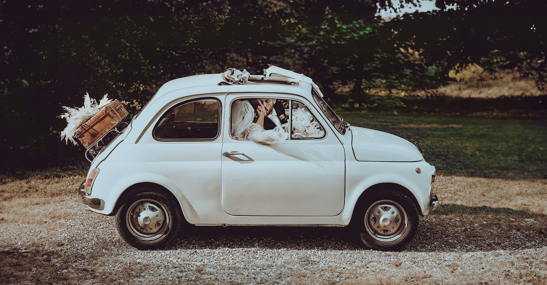 Matrimonio al Castello di Rivara. Gli sposi dopo la cerimonia, dentro la vecchia Fiat 500 bianca con tanto di valigia vintage, si baciano