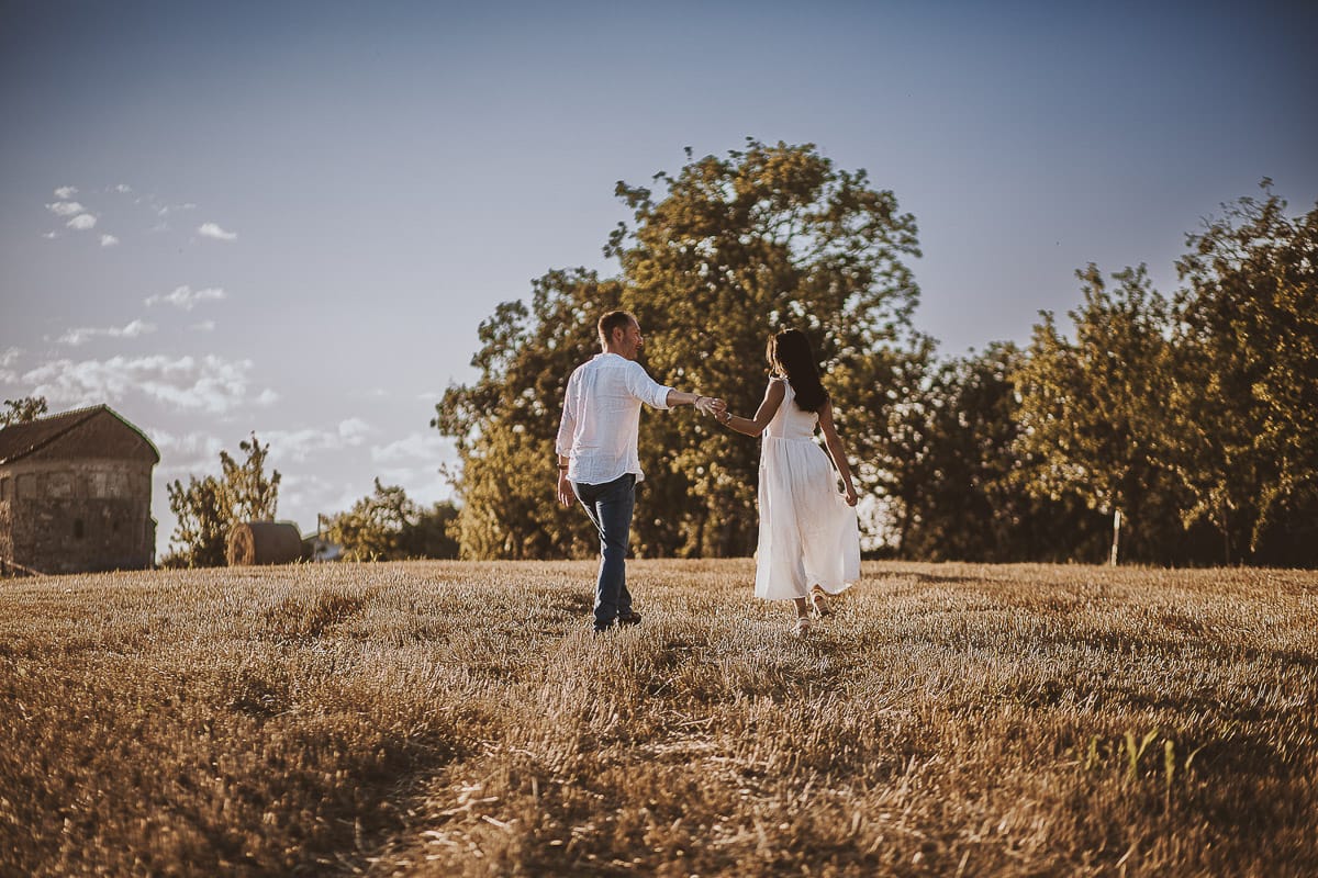 Prewedding romantico e da sogno al tramonto in Monferrato. Valeria e Omar camminano tenendosi per mano in un campo di grano tagliato.