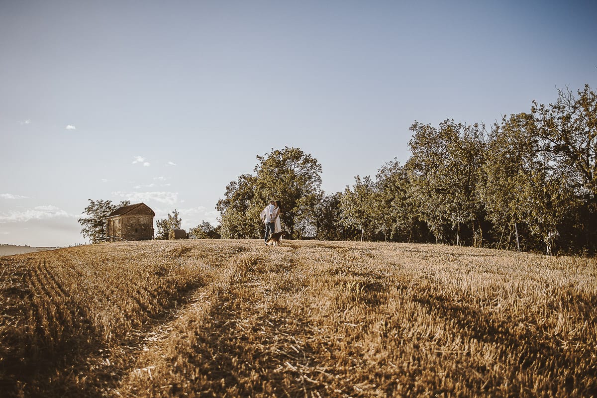 Prewedding romantico e da sogno al tramonto in Monferrato. Valeria e Omar camminano tenendosi per mano in un campo di grano tagliato.