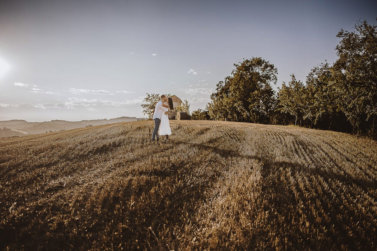 Prewedding romantico e da sogno al tramonto in Monferrato. Valeria e Omar camminano tenendosi per mano in un campo di grano tagliato.