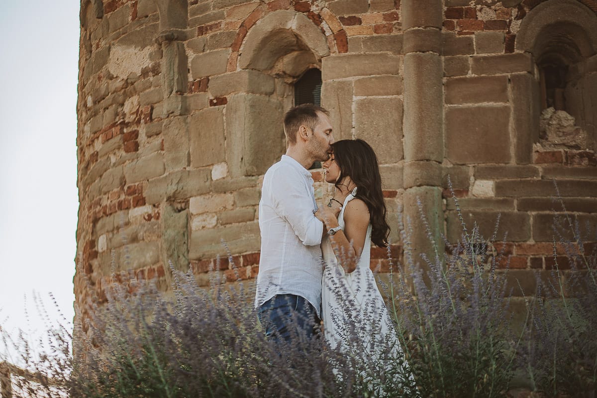 Prewedding romantico e da sogno in Monferrato. Valeria e Omar in mezzo ai fiori dietro la chiesa romanica di San Lorenzo. Omar bacia Valeria sulla fronte