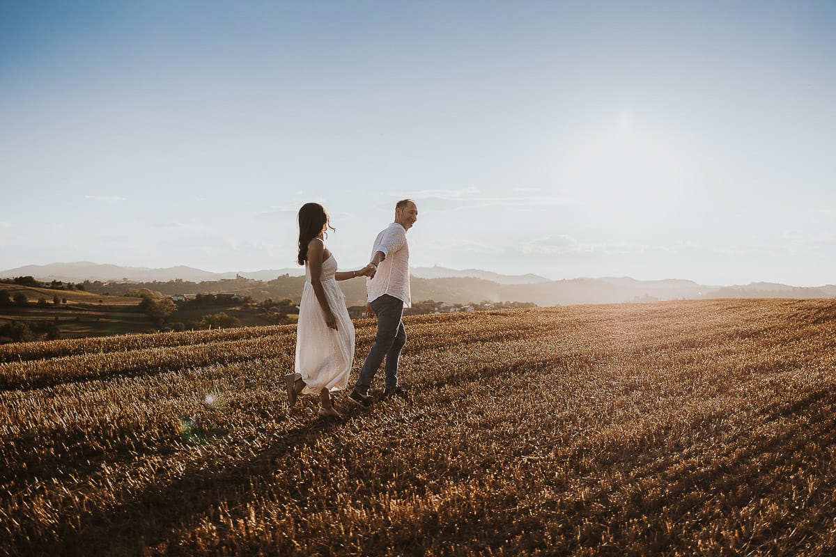Prewedding romantico e da sogno al tramonto in Monferrato. Valeria e Omar camminano in un campo di grano tagliato.