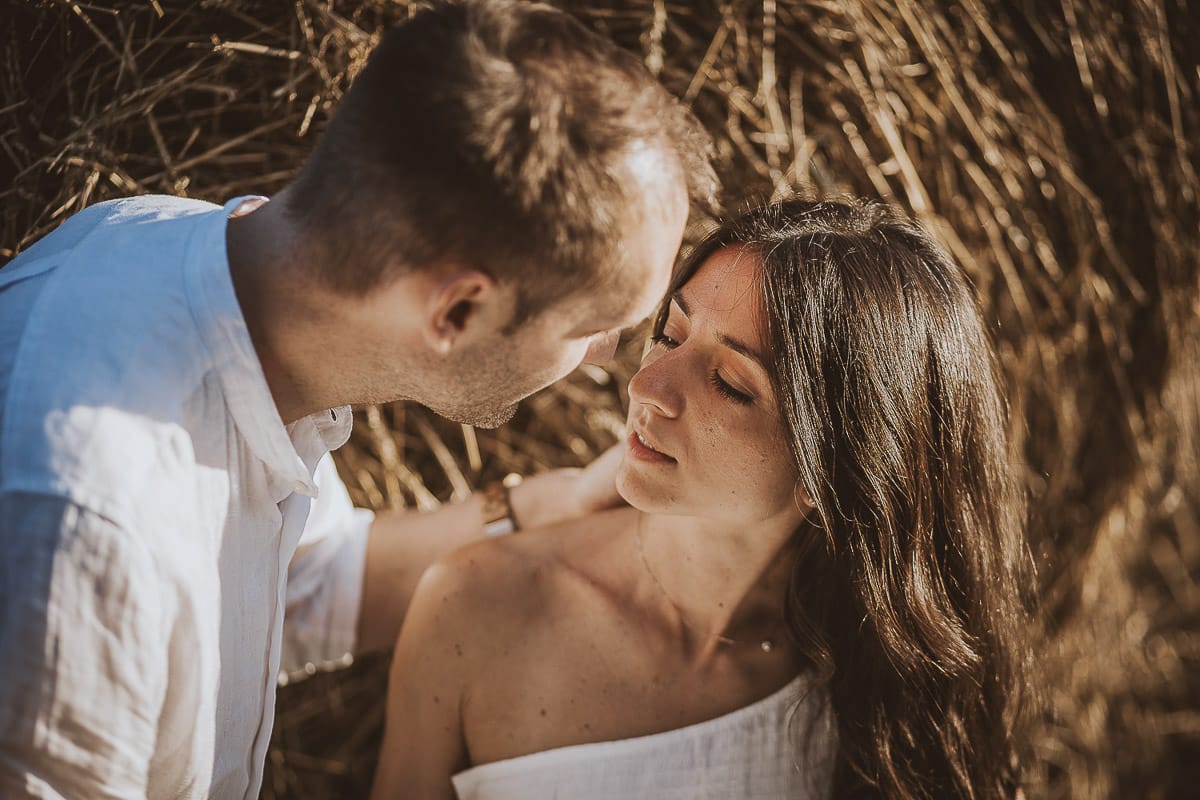 Prewedding romantico e da sogno al tramonto in Monferrato. Valeria e Omar seduti in un campo di grano tagliato vicino ad una rotoballa si guardano intensamente