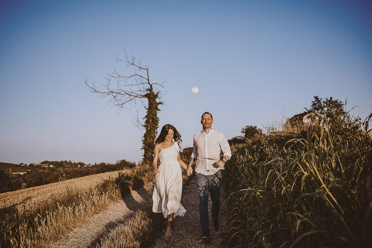 Prewedding romantico e da sogno al tramonto in Monferrato. Valeria e Omar corrono. Dietro di loro la luna piena
