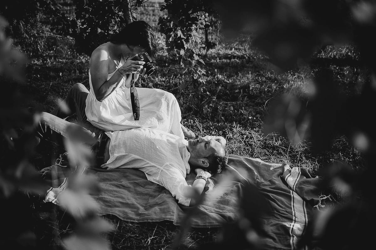 Prewedding romantico e da sogno al tramonto in Monferrato. Omar sdraiato nel vigneto. Valeria lo fotografa
