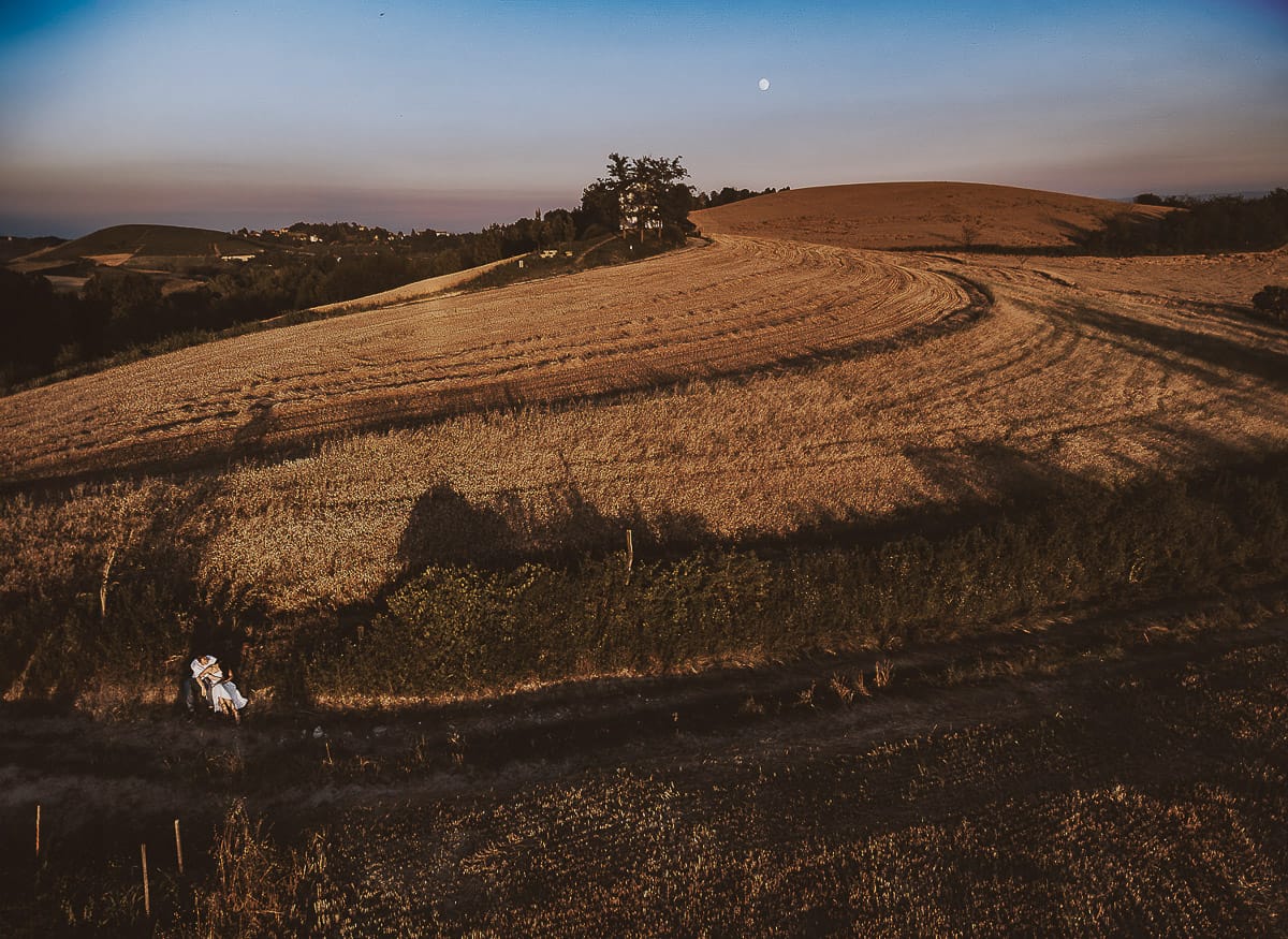 Prewedding romantico e da sogno al tramonto in Monferrato. Valeria e Omar seduti al bordo di un campo di grano. Foto aerea panoramica dal drone