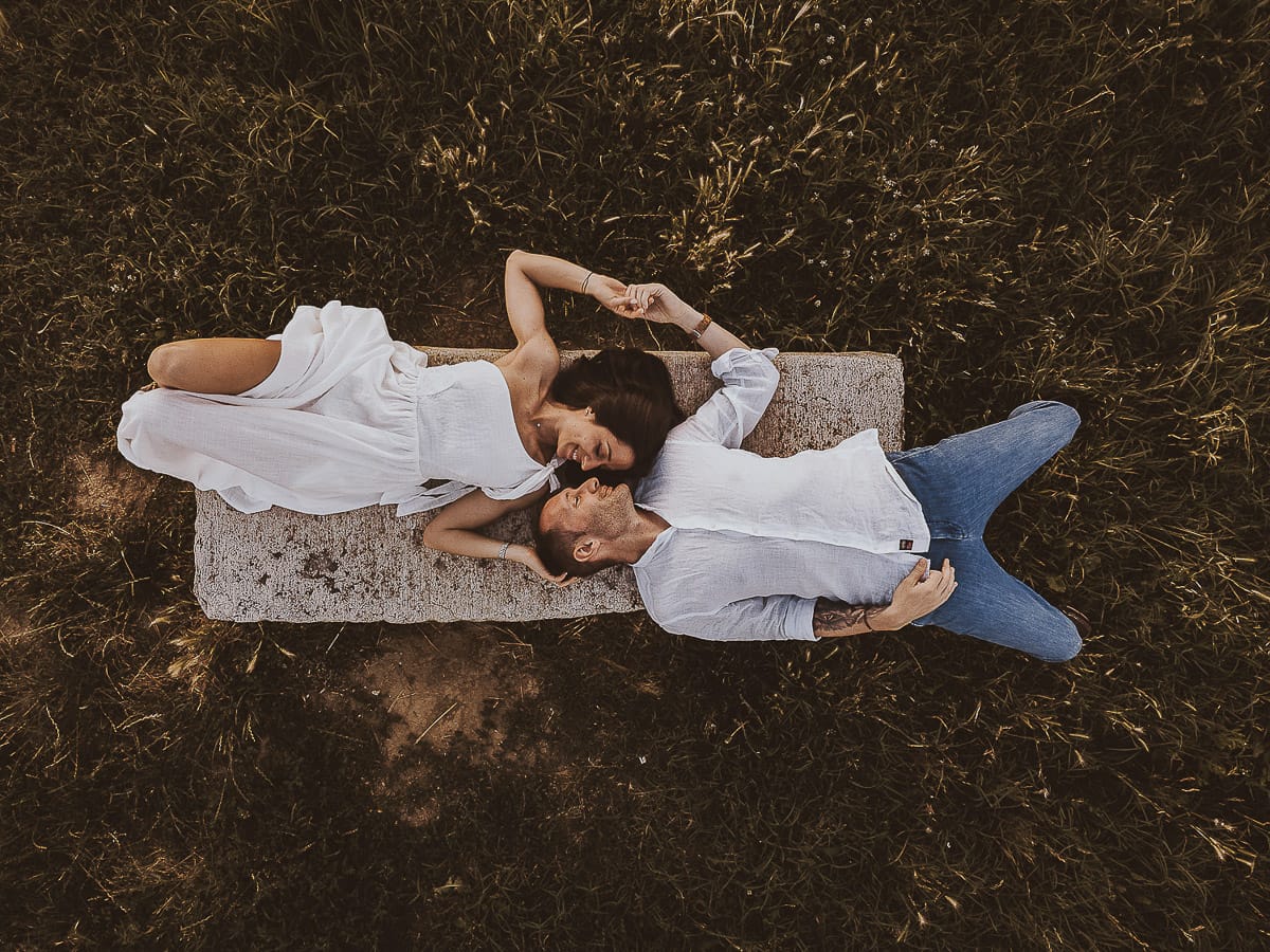 Prewedding romantico e da sogno al tramonto in Monferrato. Ritratto intenso di Valeria e Omar sdraiati su di una panchina. Foto ripresa dal drone posto sul terreno.