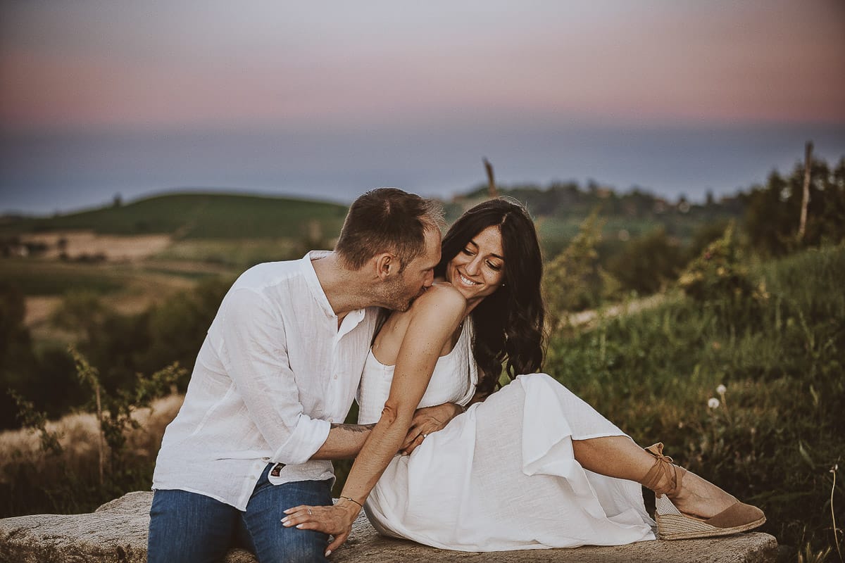 Prewedding romantico e da sogno al tramonto in Monferrato. Valeria e Omar seduti su di una panchina di pietra. Omar bacia la spalla di Valeria