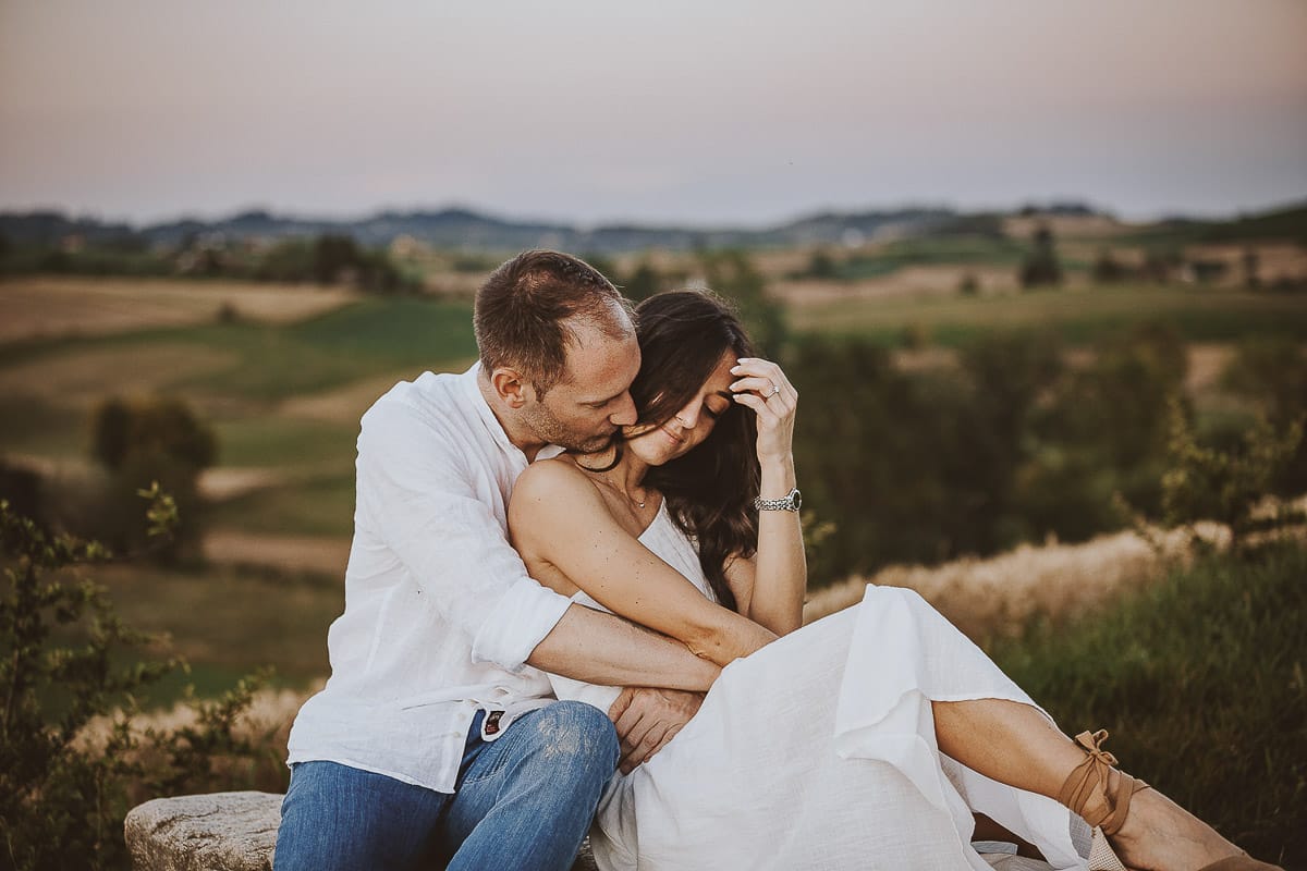 Prewedding romantico e da sogno al tramonto in Monferrato. Valeria e Omar seduti su di una panchina di pietra. Omar bacia il collo di Valeria