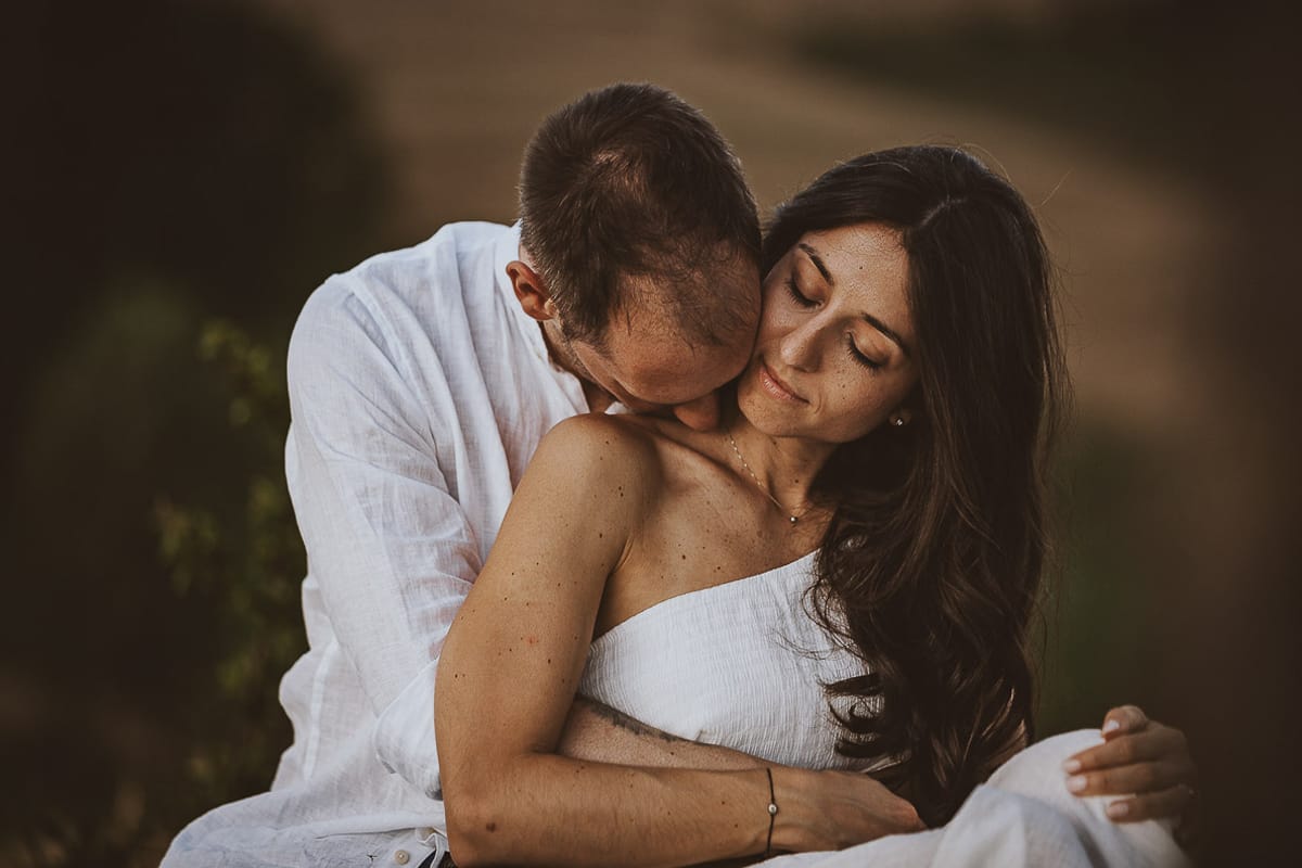 Prewedding romantico e da sogno al tramonto in Monferrato. Valeria e Omar seduti su di una panchina di pietra. Omar bacia il collo di Valeria