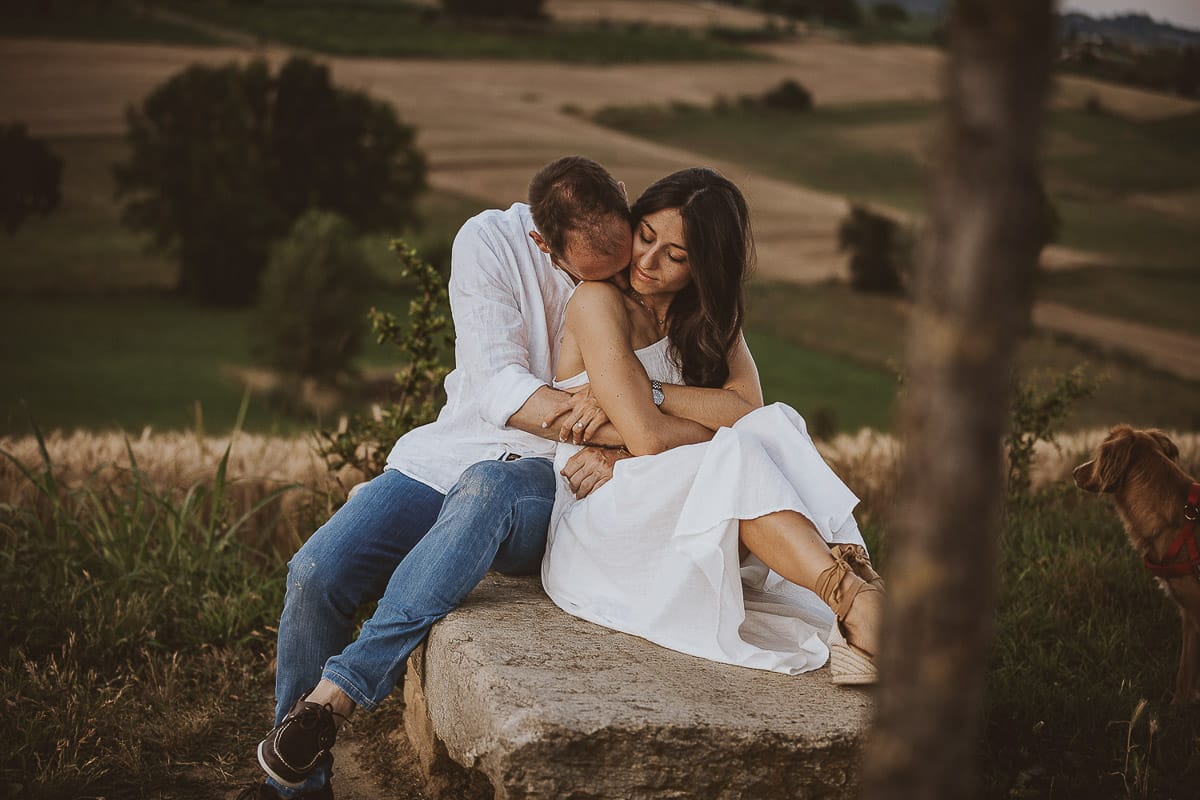 Prewedding romantico e da sogno al tramonto in Monferrato. Valeria e Omar seduti su di una panchina di pietra. Omar bacia la spalla di Valeria