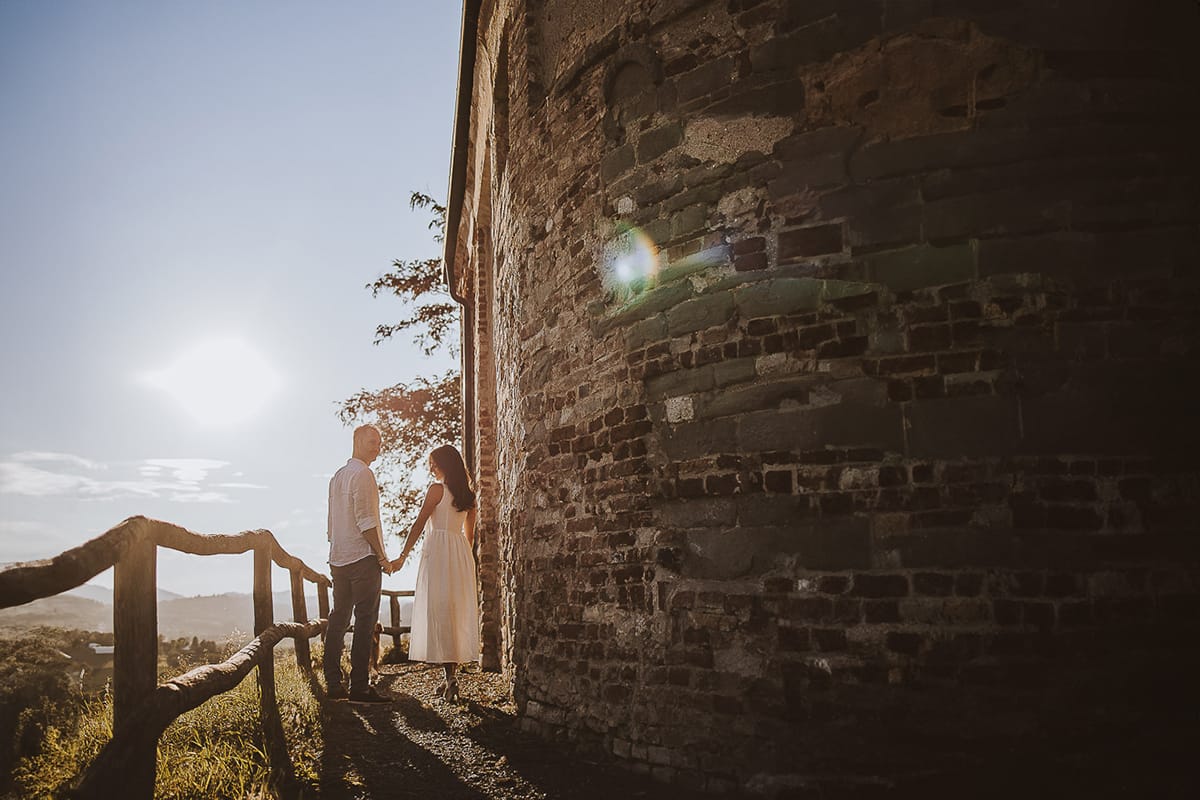 Prewedding romantico e da sogno in Monferrato. Valeria e Omar in mezzo ai fiori dietro la chiesa romanica di San Lorenzo camminano tenendosi per mano con la luce calda del tramonto