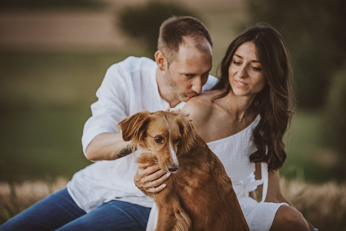 Prewedding romantico e da sogno al tramonto in Monferrato. Valeria e Omar seduti su di una panchina di pietra. Omar bacia la spalla di Valeria. C'è anche la cagnolina Nadine