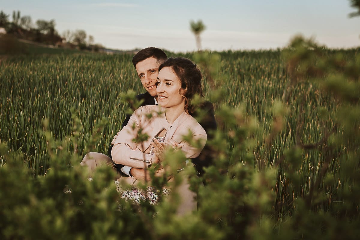 Prewedding primaverile in collina a Mombello di Torino di Federica e Mattia. Federica e Mattia sono seduti in un campo di grano ancora verde.