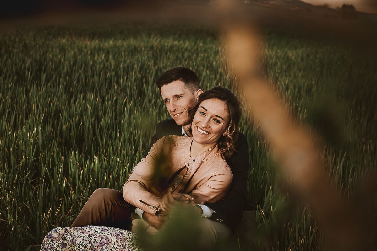 Prewedding primaverile in collina a Mombello di Torino di Federica e Mattia. Federica e Mattia sono seduti in un campo di grano ancora verde.