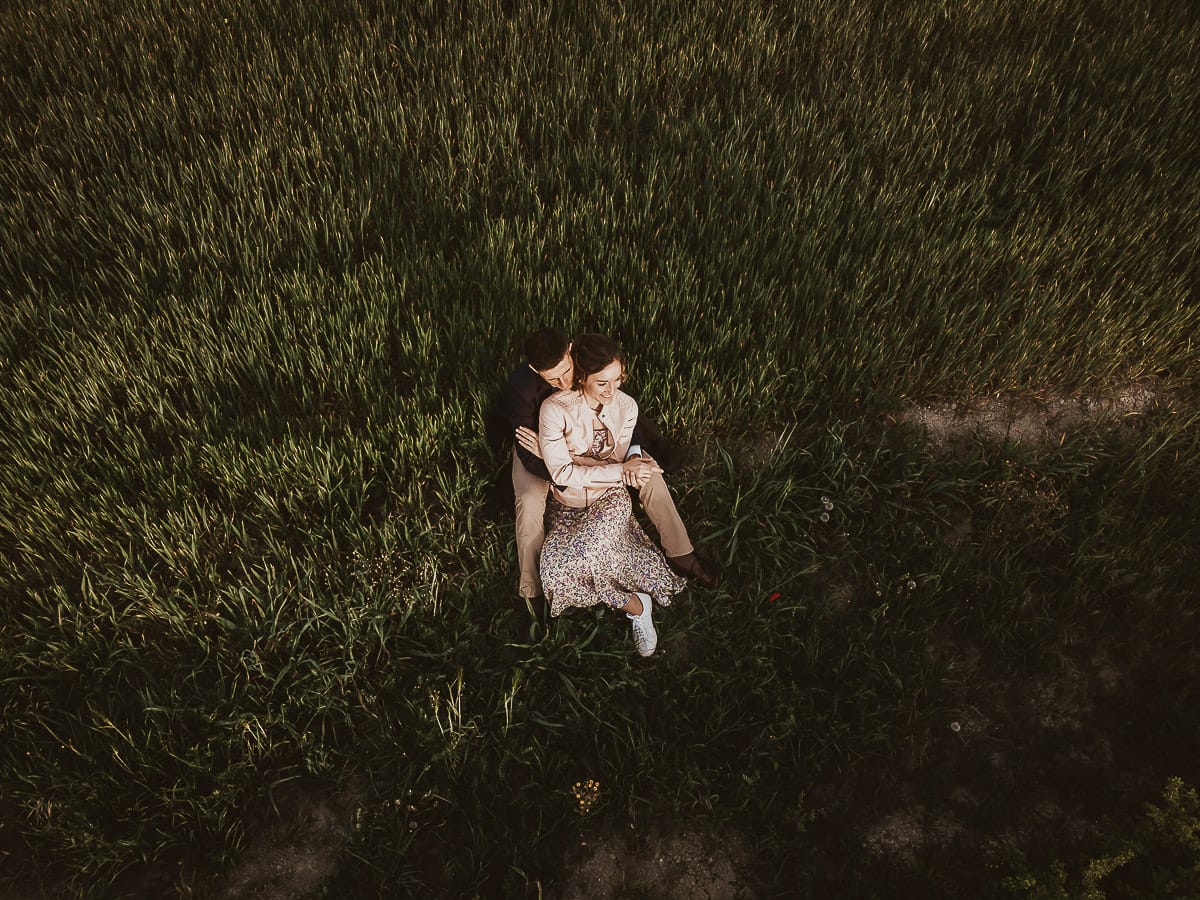 Prewedding primaverile in collina a Mombello di Torino di Federica e Mattia. Federica e Mattia sono seduti in un campo di grano ancora verde. Foto dal drone.