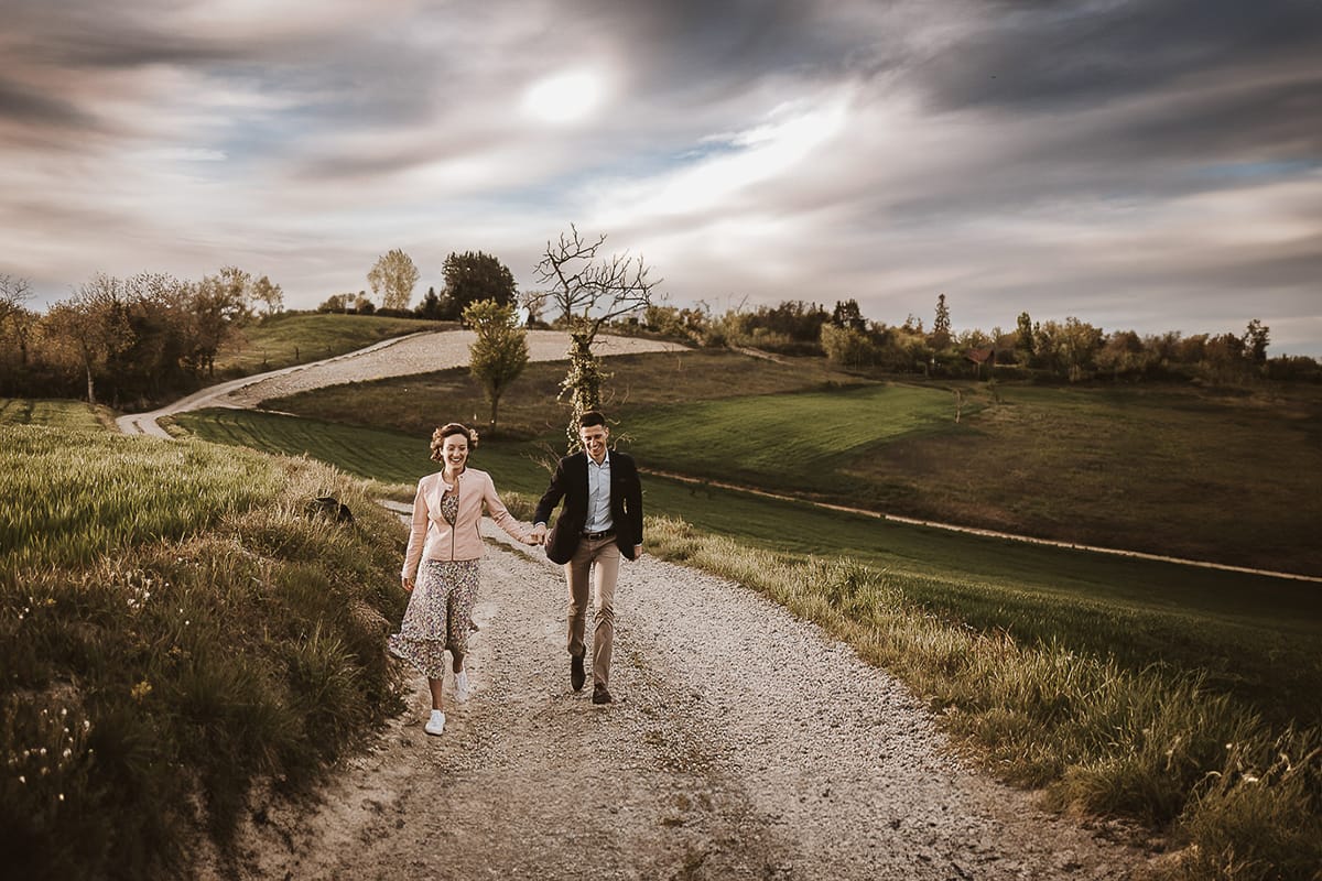Prewedding primaverile in collina a Mombello di Torino di Federica e Mattia. Federica e Mattia camminano. Dietro il cielo nuvoloso è bellissimo.