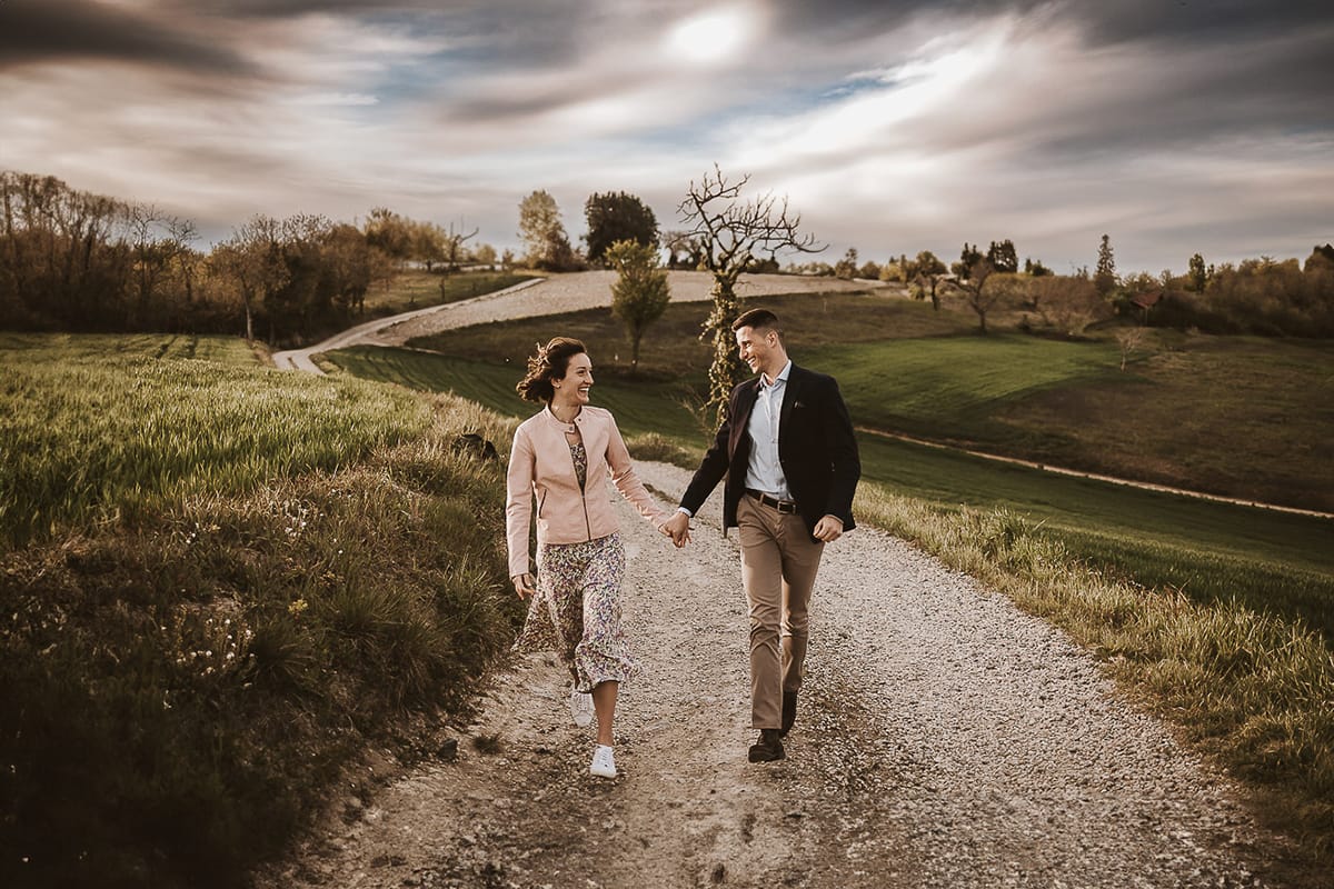 Prewedding primaverile in collina a Mombello di Torino di Federica e Mattia. Federica e Mattia corrono. Dietro il cielo nuvoloso è bellissimo.