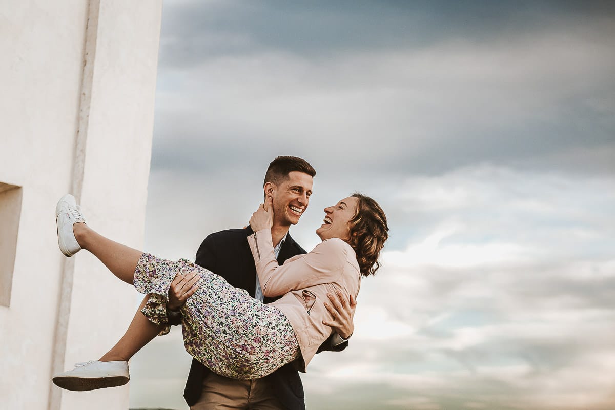 Prewedding primaverile in collina a Mombello di Torino di Federica e Mattia. Federica e Mattia di fronte alla chiesa di San Lorenzo. Mattia prende in braccio Federica.