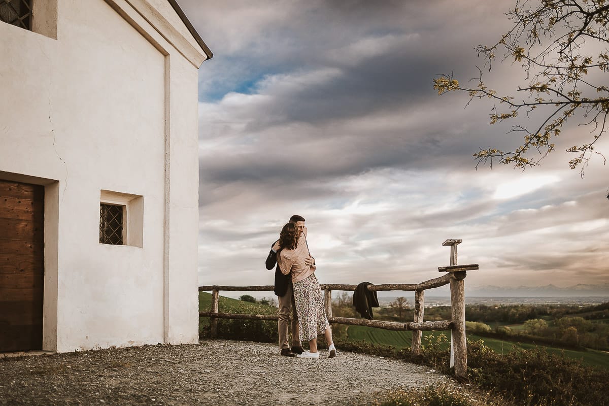 Prewedding primaverile in collina a Mombello di Torino di Federica e Mattia. Federica e Mattia di fronte alla chiesa di San Lorenzo. Mattia e Federica si abbracciano