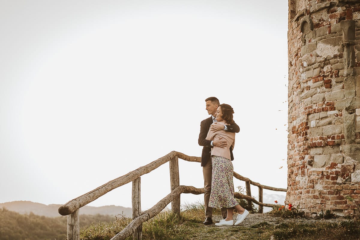 Prewedding primaverile in collina a Mombello di Torino di Federica e Mattia. Federica e Mattia di fronte alla chiesa di San Lorenzo. Mattia e Federica si abbracciano guardando il panorama.