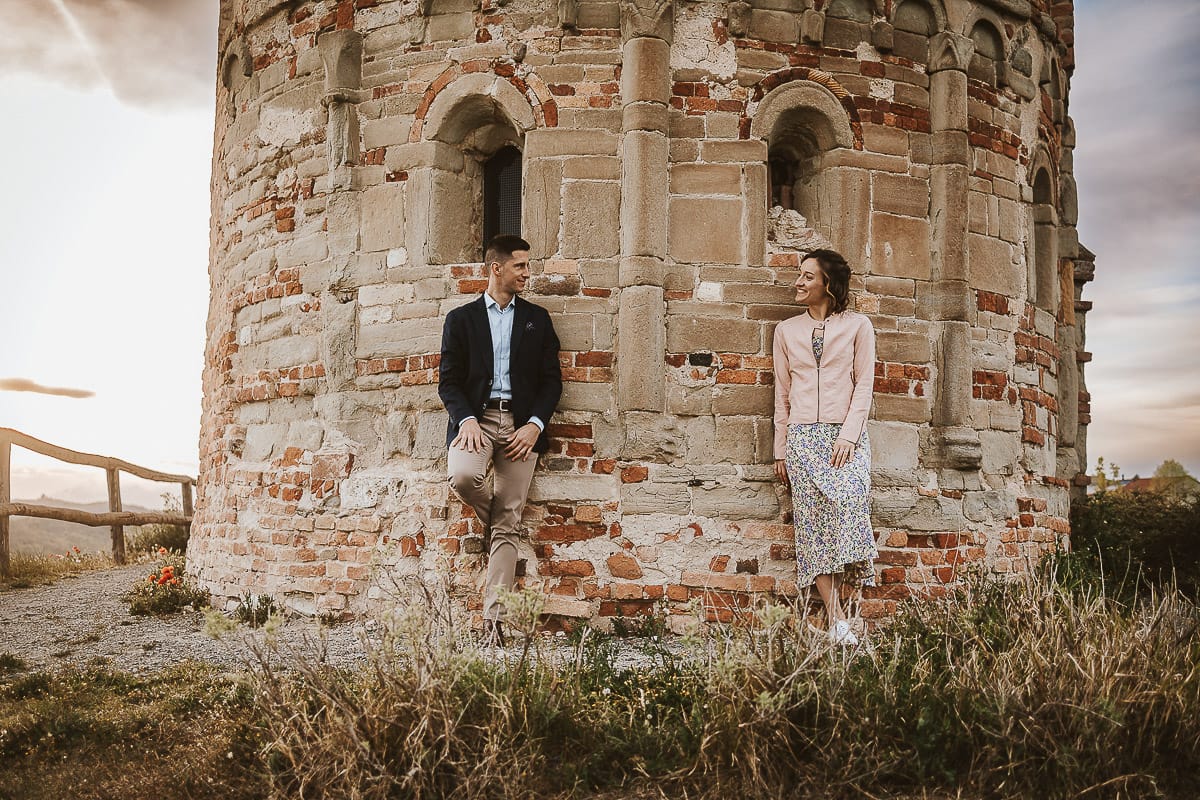 Prewedding primaverile in collina a Mombello di Torino di Federica e Mattia. Federica e Mattia di fronte alla chiesa di San Lorenzo. Mattia e Federica appoggiati al muro della chiesa romanica.
