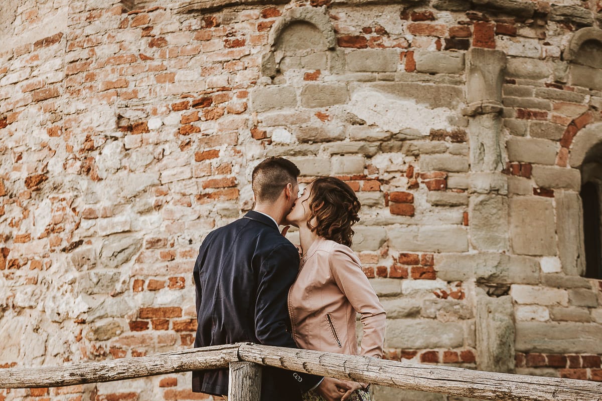 Prewedding primaverile in collina a Mombello di Torino di Federica e Mattia. Federica e Mattia di fronte alla chiesa di San Lorenzo.Federica bacia Mattia sulla guancia.