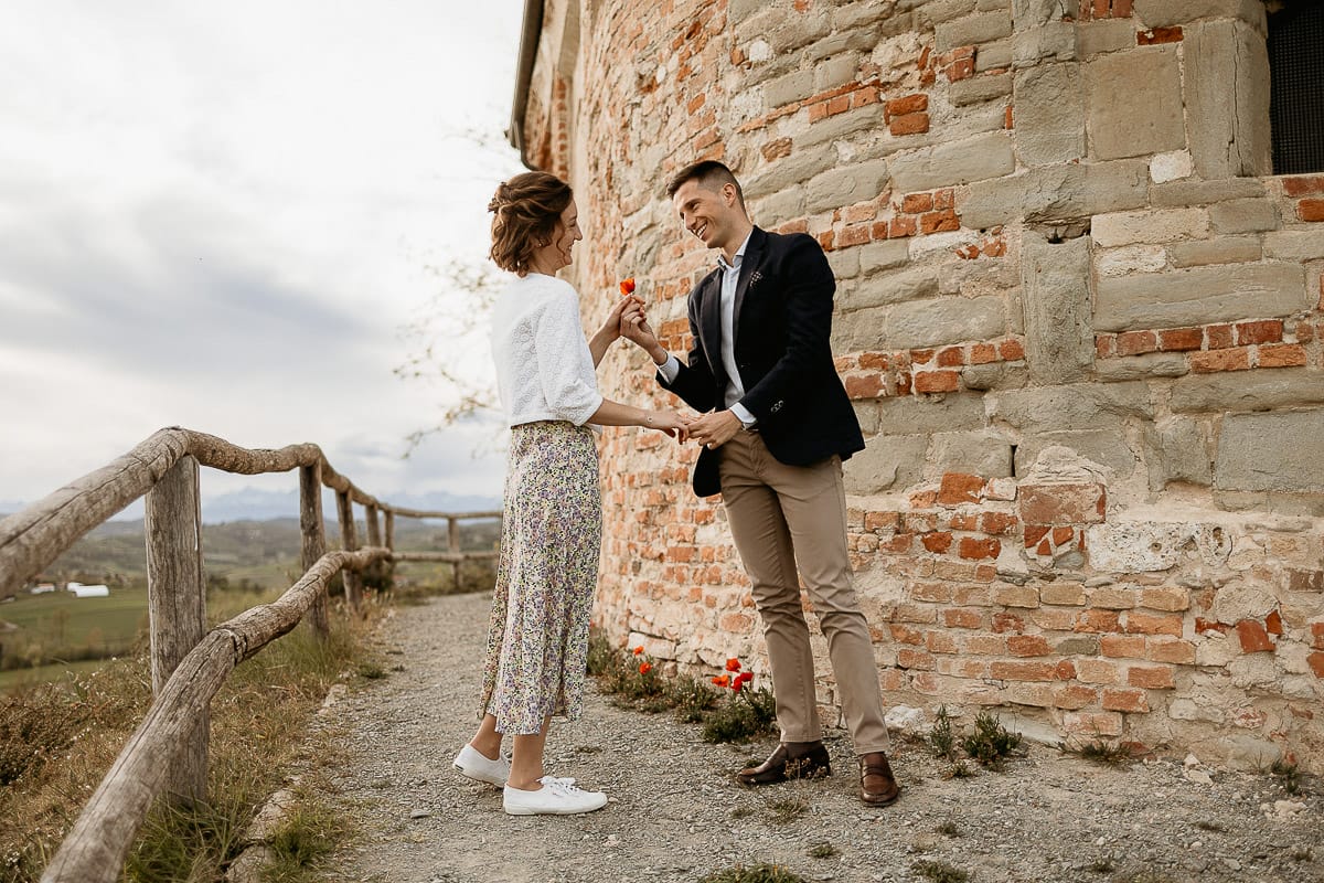 Prewedding primaverile in collina a Mombello di Torino di Federica e Mattia. La coppia si tiene per mano. Mattia porge un papavero a Federica.