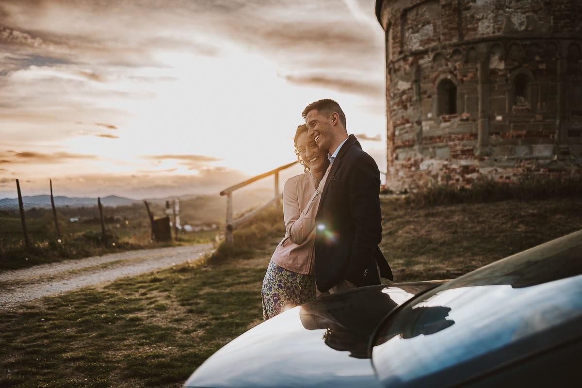 Prewedding primaverile in collina a Mombello di Torino di Federica e Mattia. Federica e Mattia dietro la BMW vintage di Mattia riflessi nell'auto.