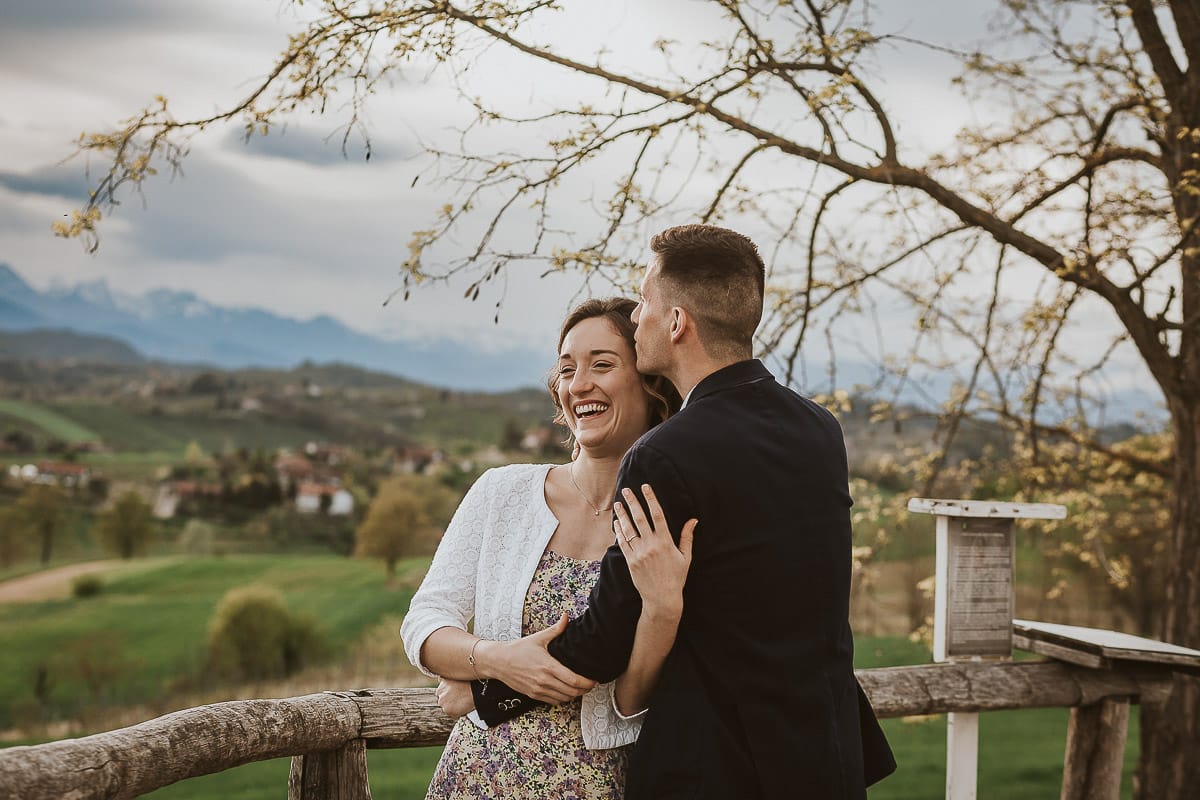Prewedding primaverile in collina a Mombello di Torino di Federica e Mattia. Mattia bacia Federica sulla tempia. Federica rida